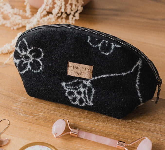 Black pouch with white floral patterns on a wooden surface with beauty tools.